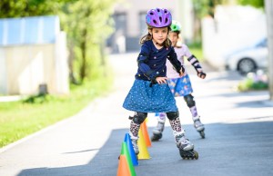 Children learning to roller skate on the road with cones. Twin girls are practising safe roller skating on a home driveway road wearing protective gear - helmets, knee, elbow and hand protectors or pads.